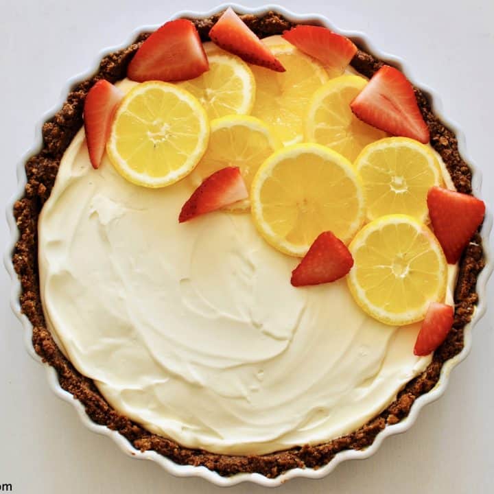 overhead shot of a no-bake lemon cheesecake decorated with slices of lemon and strawberries with a chocolate hobnob crust