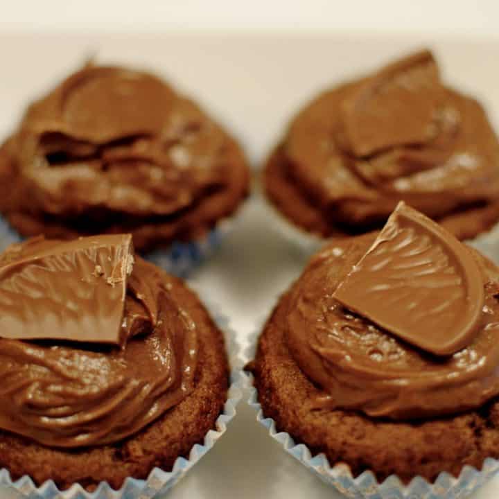 4 chocolate orange cupcakes in a bowl, topped with chocolate buttercream and a piece of chocolate orange.