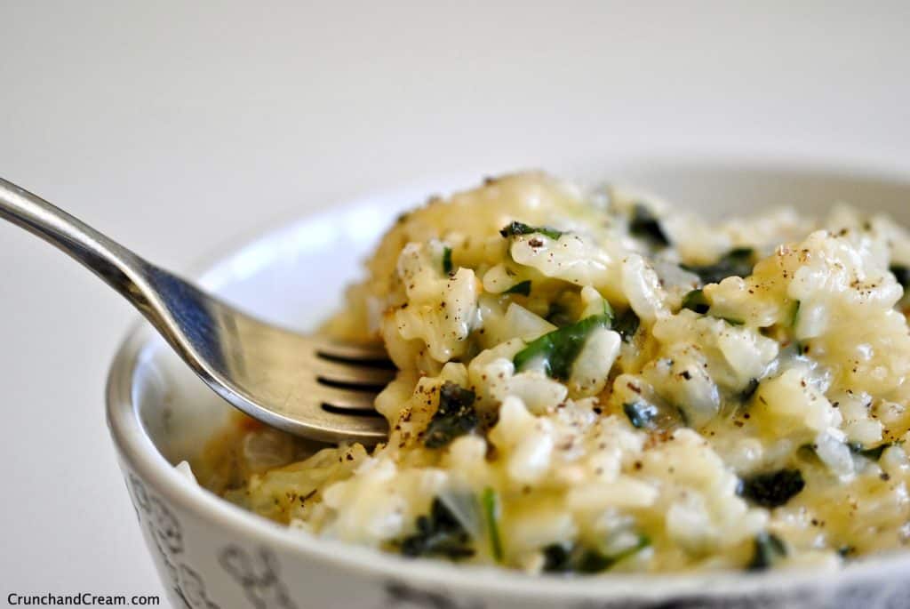 A close-up of a bowl full of creamy risotto with chopped green herbs in.
