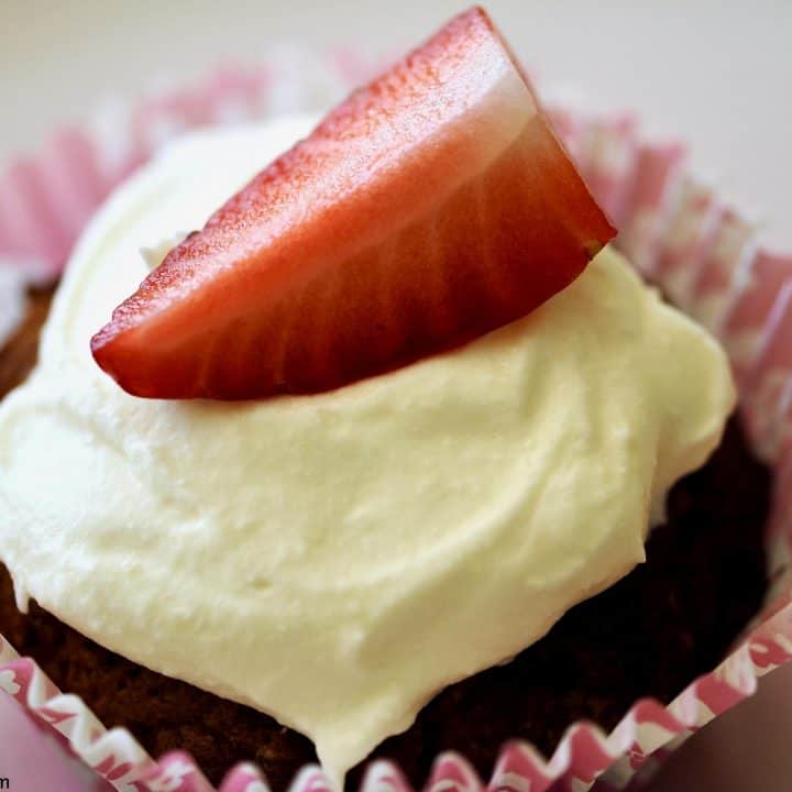 Close-up of an individual strawberry cupcake topped with smooth white chocolate cream cheese icing and a slice of strawberry.