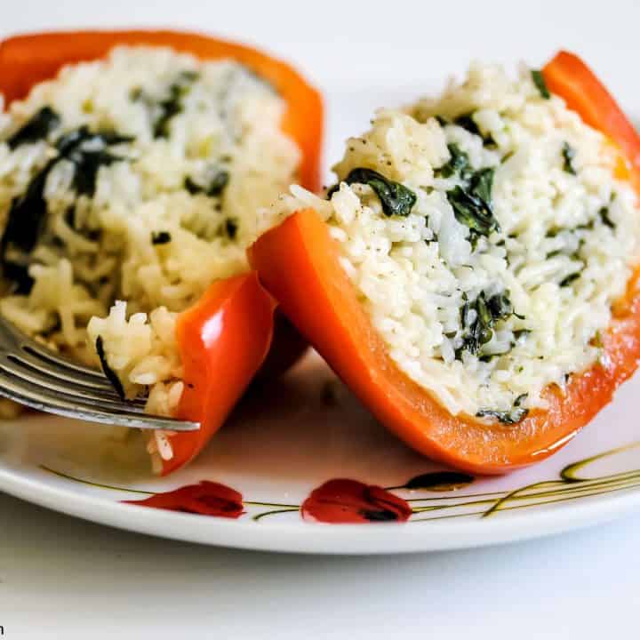 halved stuffed pepper on a plate full of cheesy basil and spinach rice. A fork is taking a bite-size piece of the pepper.