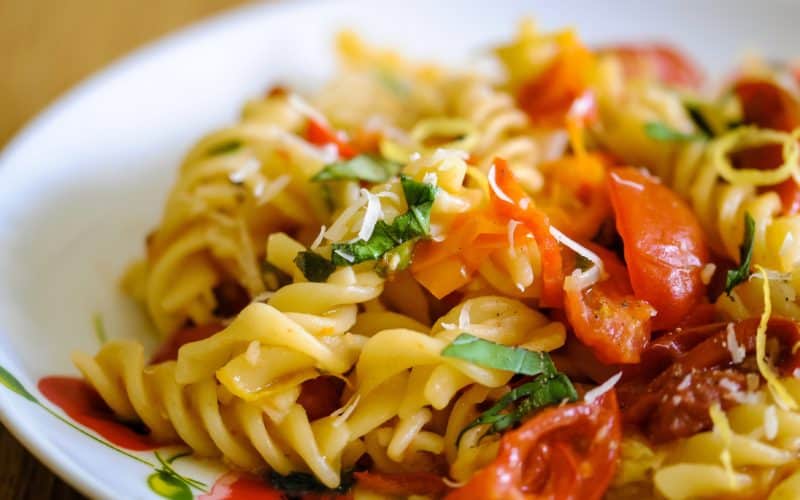 close-up eye-level photo of a plate of fusilli pasta cooked with fresh tomatoes and chilli peppers, topped with lemon zest and chopped fresh herbs