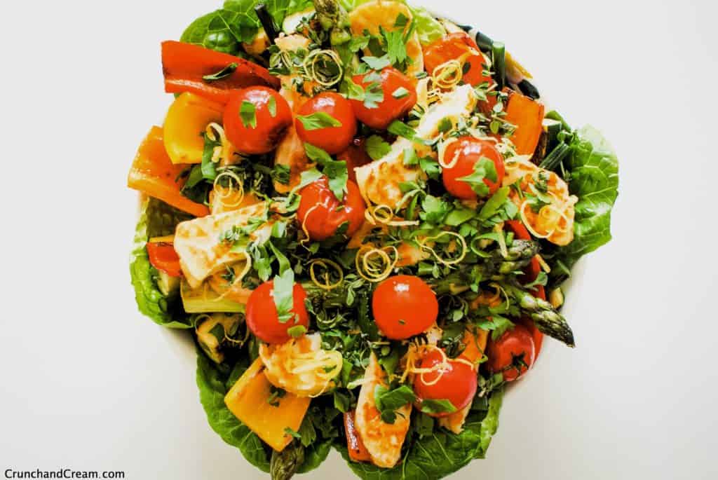overhead of grilled halloumi salad with lettuce, tomatoes, peppers, lemon zest and herbs