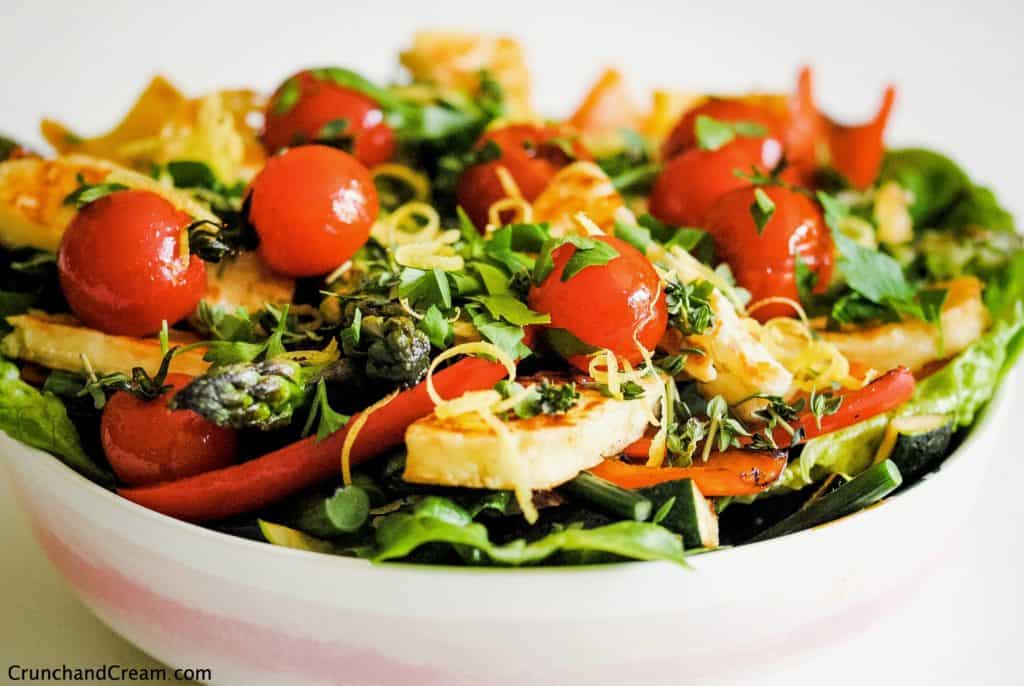 bowl of halloumi salad with halloumi slices, grilled tomatoes and peppers, lettuce, lemon zest and herbs