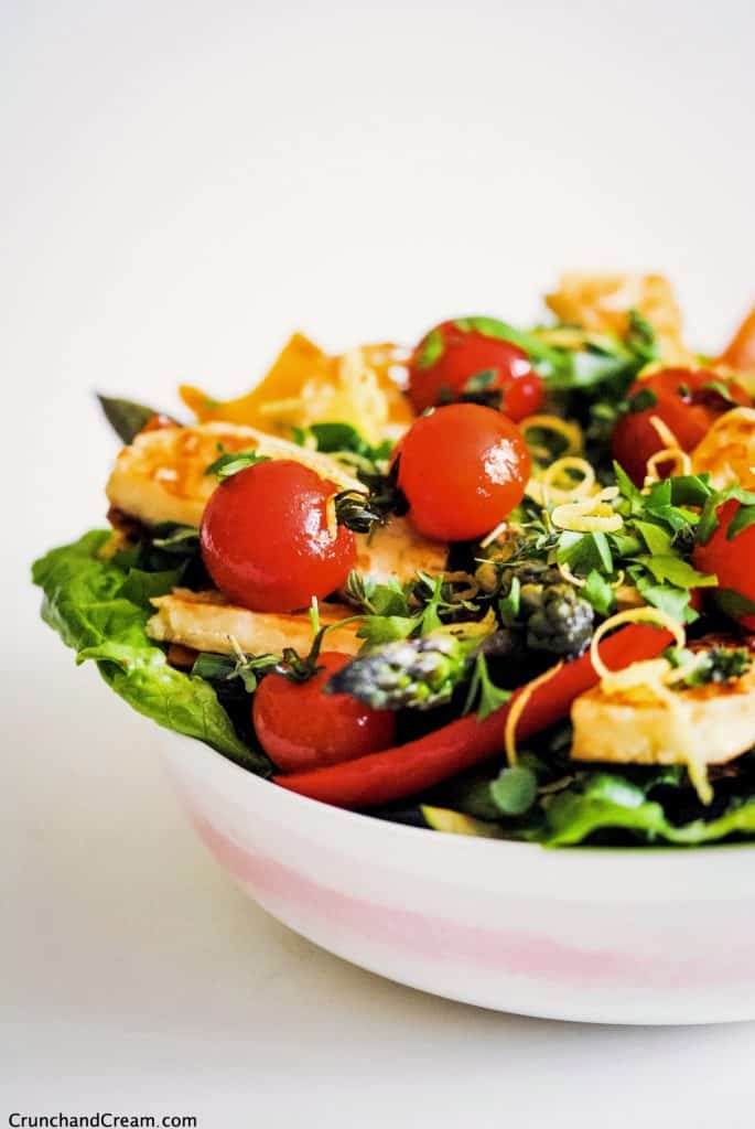 bowl of halloumi salad with halloumi slices, grilled tomatoes and peppers, lettuce, lemon zest and herbs