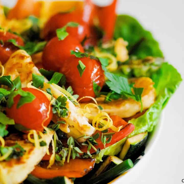 close-up of halloumi salad with grilled tomatoes and peppers as well as lettuce, herbs and lemon zest