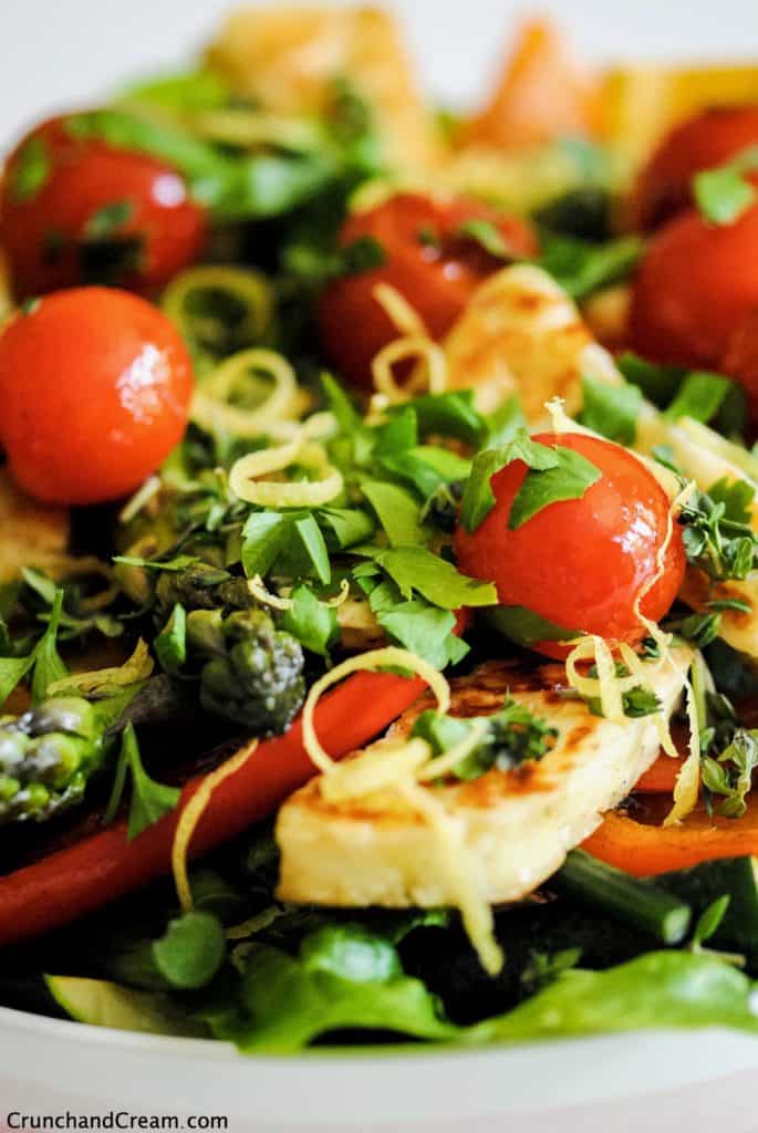 close-up of halloumi salad with grilled tomatoes and peppers as well as lettuce, herbs and lemon zest
