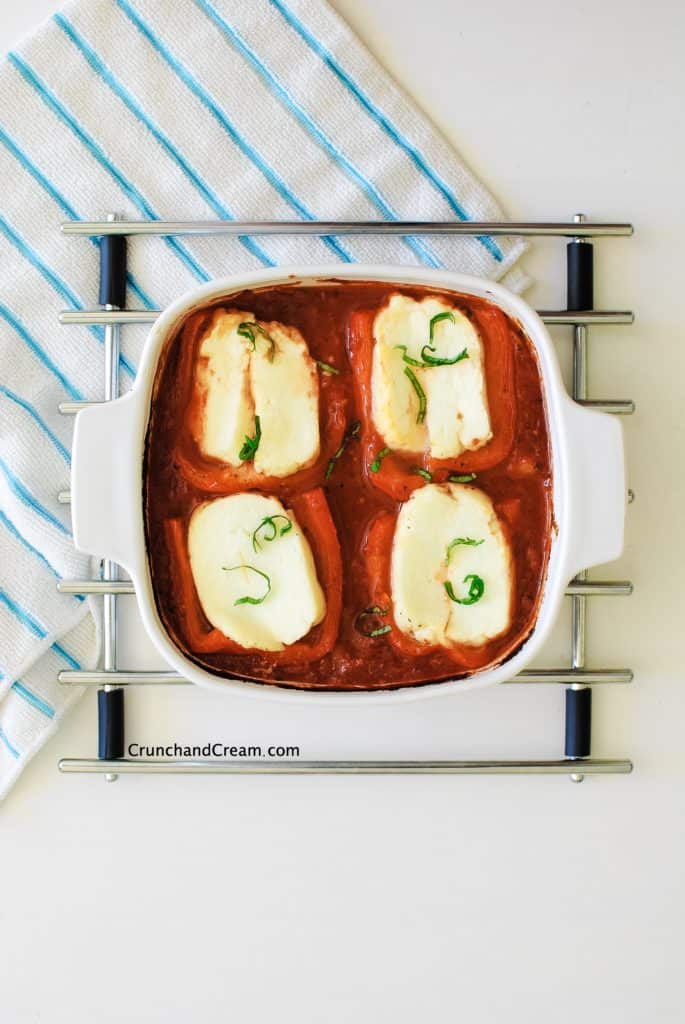 a tray full of tomato sauce, red pepper halves and halloumi slices on a white background