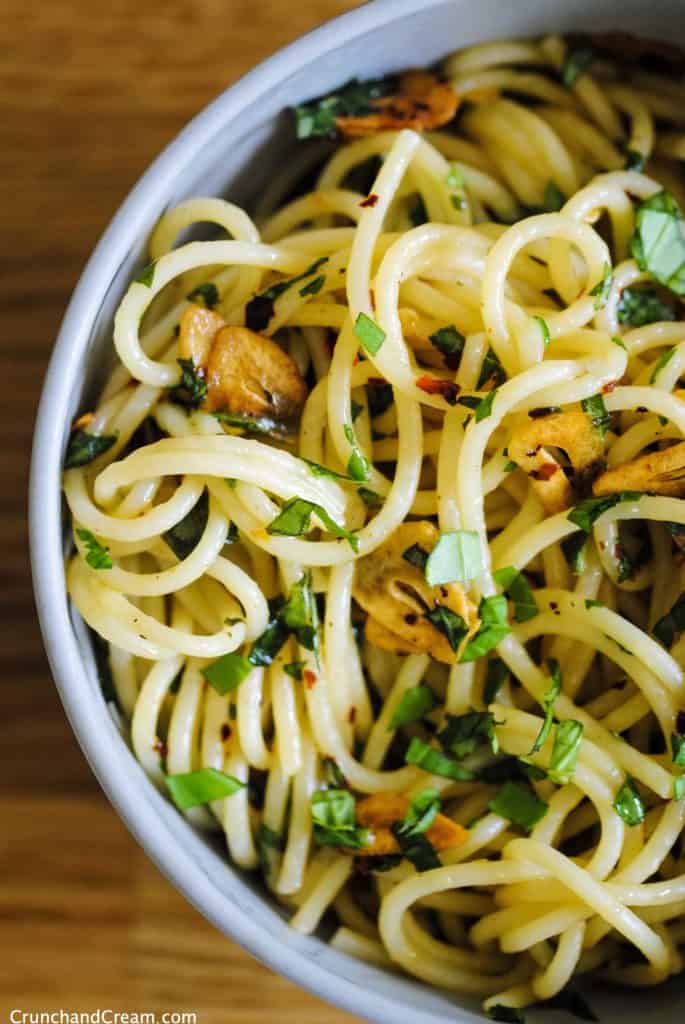 overhead of spaghetti with finely chopped fresh basil, chilli flakes, and thinly sliced garlic