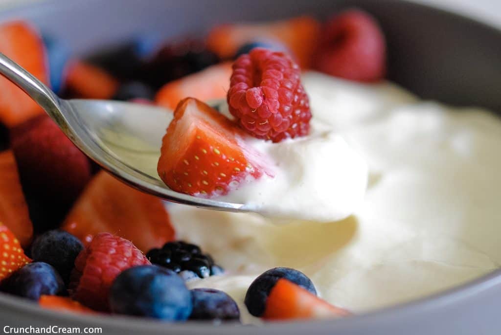 a spoon holding fresh berries and creamy cheesecake mix, with more of both in a bowl in the background
