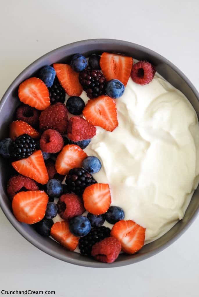 overhead photo of a bowl with mixed fresh berries on one side and cheesecake mix on the other