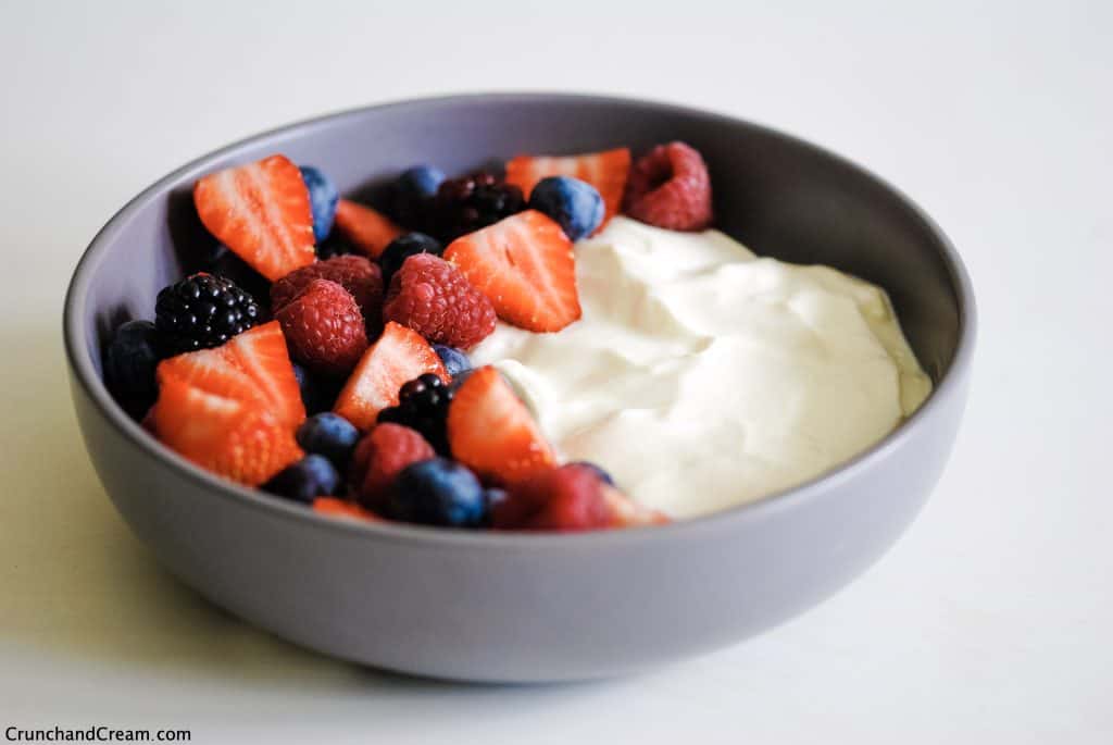 a grey bowl with colourful fresh berries on the left and smooth white cheesecake mixture on the right