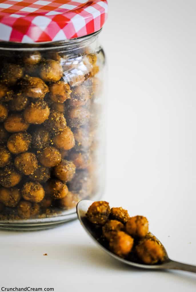 a spoonful of indian chickpeas on a white table in front of a jar full of crispy indian chickpeas