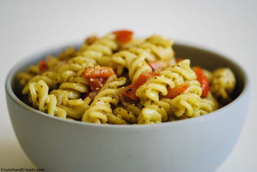a bowl of pesto pasta with diced red pepper on a white background