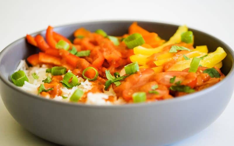 A bowl of rice and colourful vegetables drizzled with red enchilada sauce