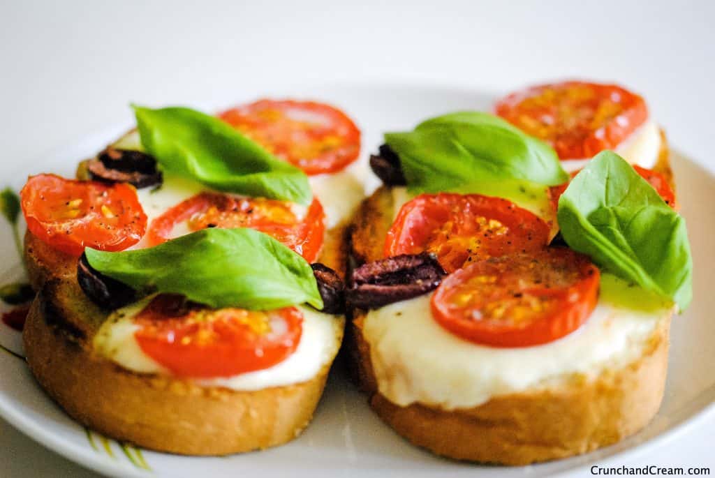 two slices of toast with cheese, tomatoes, olives and basil