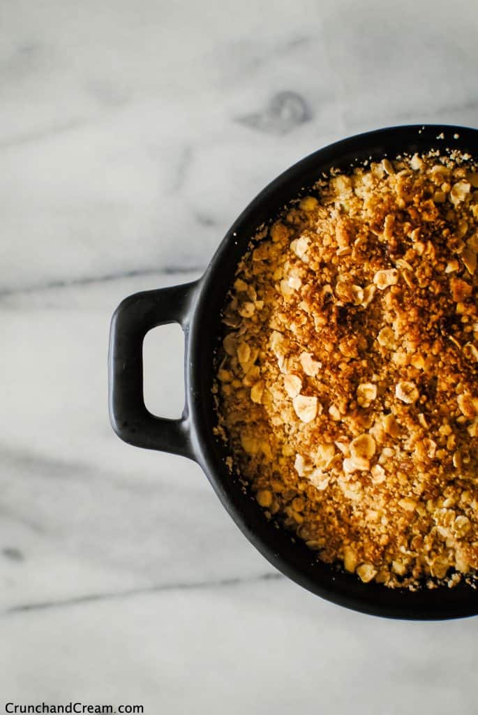 close-up overhead of a round, black dish of apple crumble with a crispy, golden-brown topping