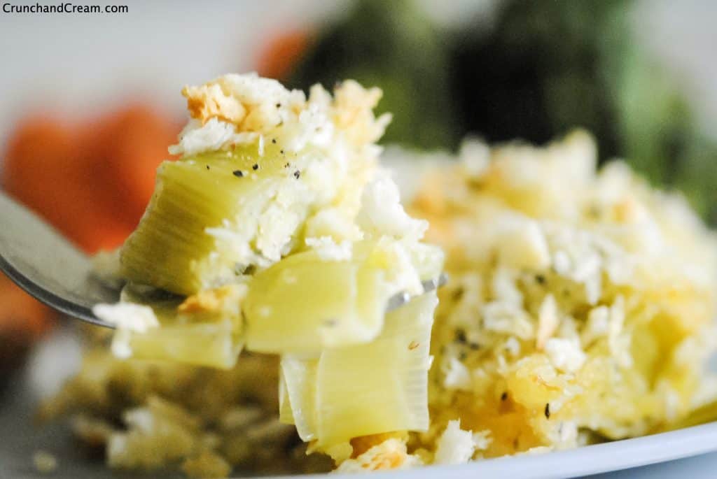 a forkful of creamy, cheesy leeks with steamed veggies in the background
