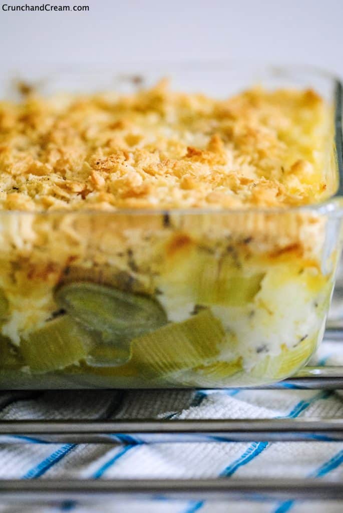 a clear dish of creamy leeks topped with breadcrumbs on a metal rack and kitchen towel