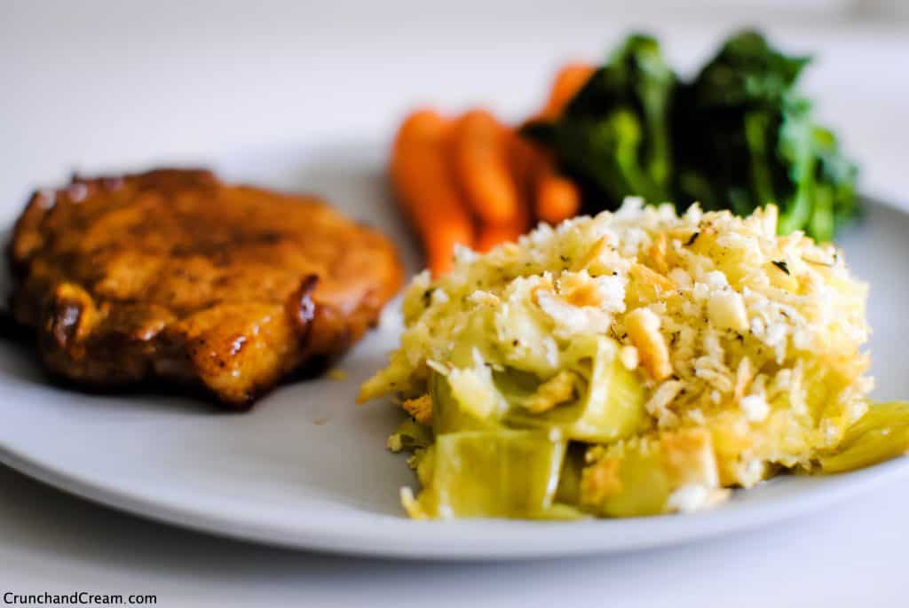 plate of cheesy, creamy leeks with golden breadcrumbs. Pork chop and steamed vegetables on the side.