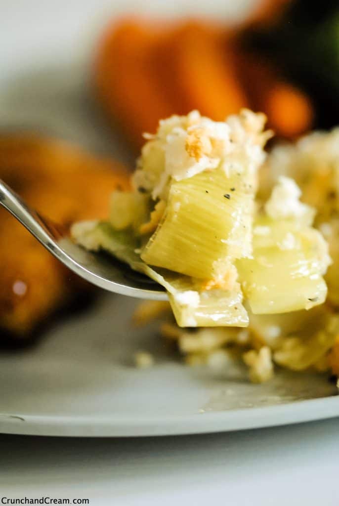 a forkful of leek bake with pork chop and steamed veggies in the background