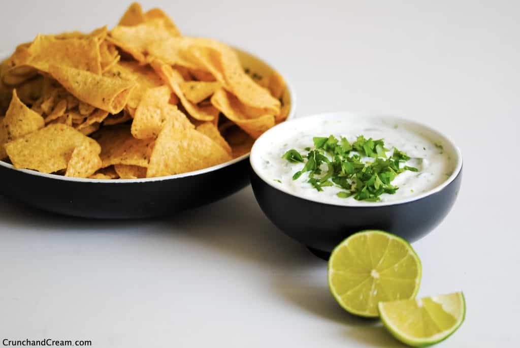 a bowl of coriander lime dipping sauce with a sliced lime and a bowl of tortilla chips