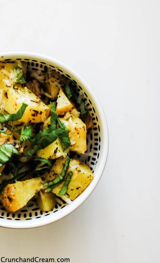 Overhead of a bowl full of yellow potatoes topped with grated cheese and fresh herbs.