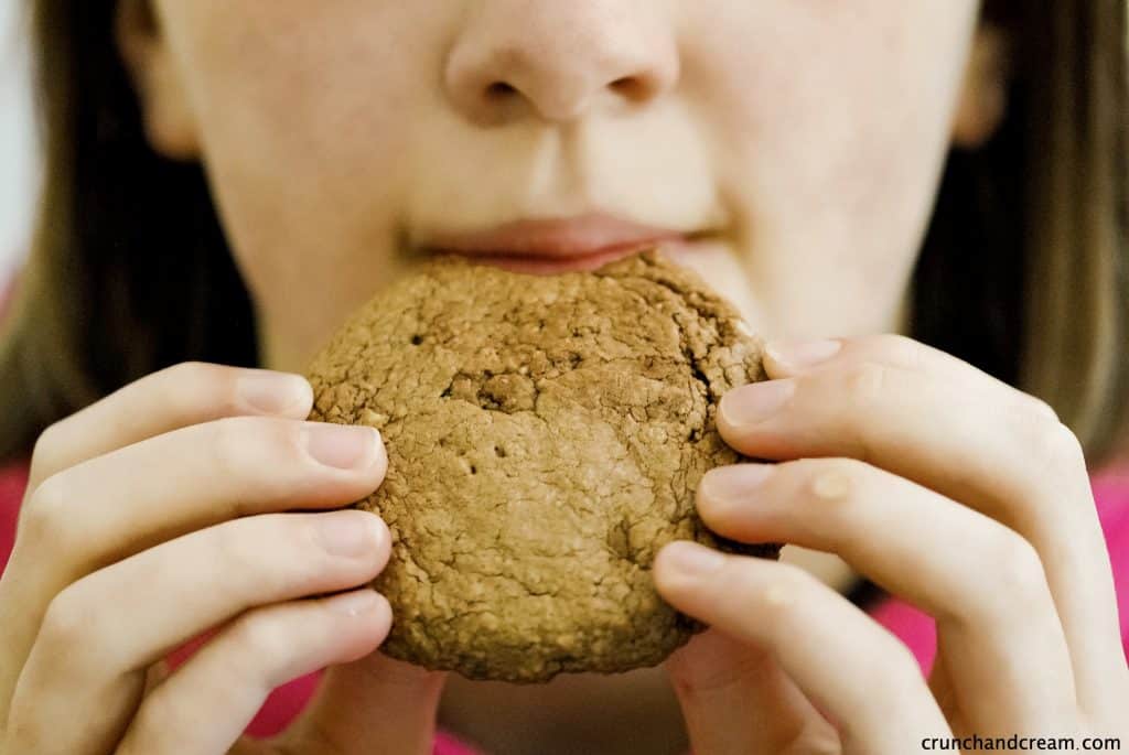 a young girl about to take a bite of a brown nutella cookie