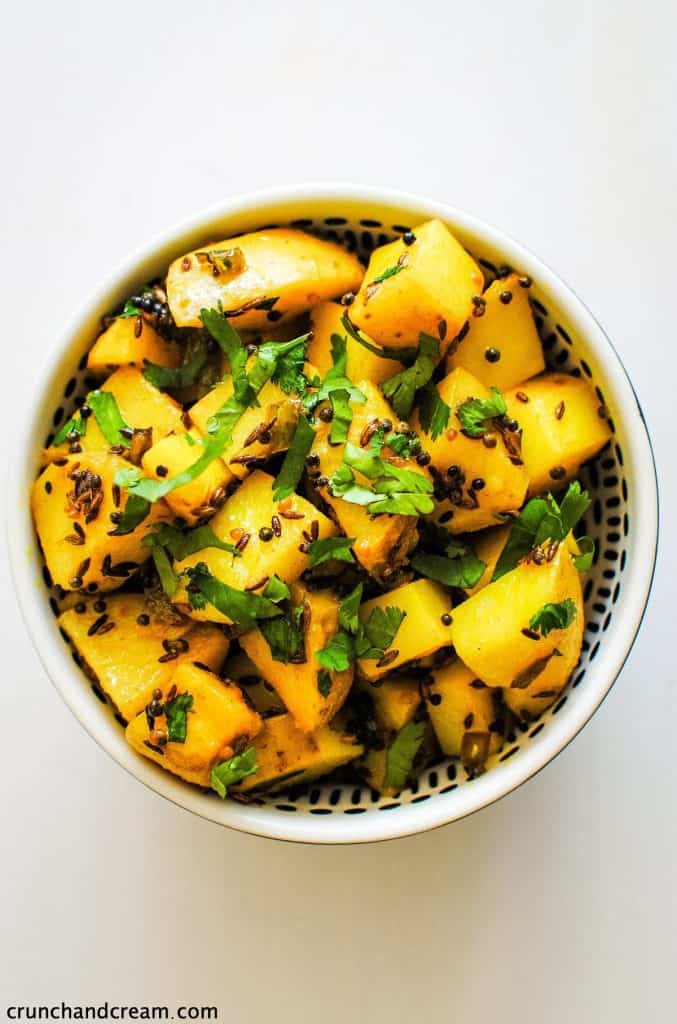 overhead of a black bowl full of yellow spiced cubes of potato