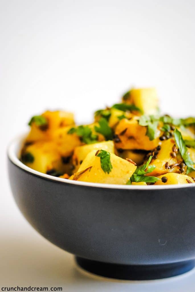 a black bowl of yellow spiced potatoes topped with fresh green herbs