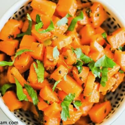 bowl of carrot pieces (overhead) with some fresh herbs and small whole spices