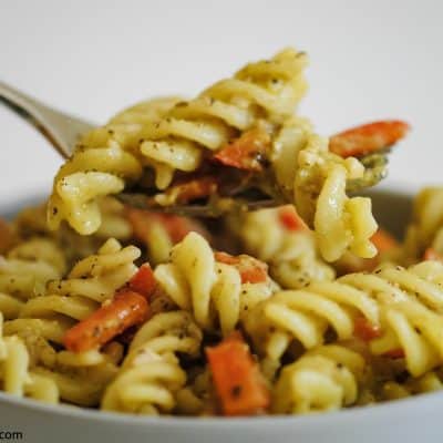 a fork full of a bowl of pesto pasta with diced red pepper