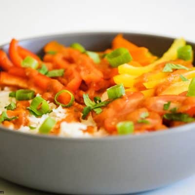 A bowl of rice and colourful vegetables drizzled with red enchilada sauce
